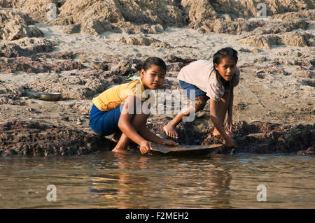 Horizontal portrait of two young girls panning for gold at the edge of the Mekong river. Stock Photo