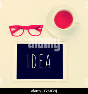 high-angle shot of a table with a pair of red plastic-rimmed eyeglasses, a cup of tea and a tablet computer with the word idea i Stock Photo