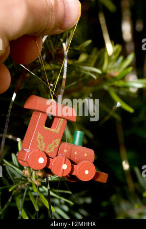close up detail of a mans hand hanging a small wooden toy steam engine on a traditional christmas tree Stock Photo