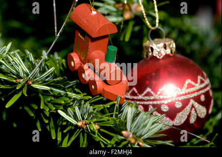 close up detail of a wooden toy steam engine and red and silver decorated bauble hanging on a traditional christmas tree Stock Photo