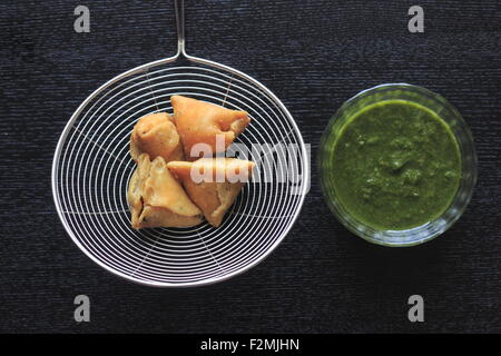Popular indian, asian and african deep fried snack called samosa with spicy chutney and mint Stock Photo