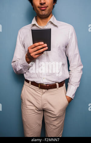 Young man standing by a blue wall and reading from tablet Stock Photo