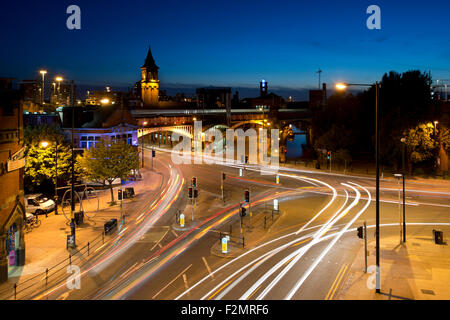 Light trails of moving traffic at the junction of Whitworth Street West and Deansgate in Manchester city centre at night. Stock Photo