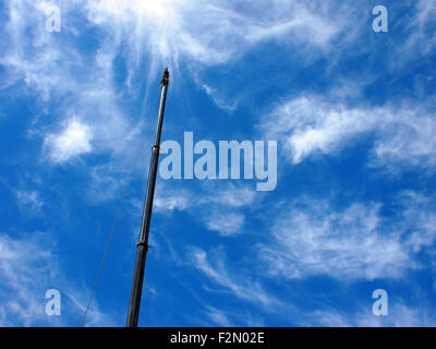 Upward view on the boom of a crane against the blue sky with white cirrus clouds Stock Photo