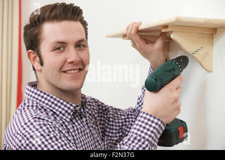 Man Putting Up Wooden Shelf At Home Using Electric Drill Stock Photo