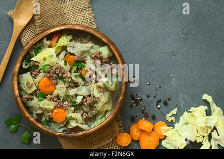 Savoy cabbage, carrot, potato and mincemeat stew or thick soup with parsley in wooden bowl, ingredients on the side Stock Photo