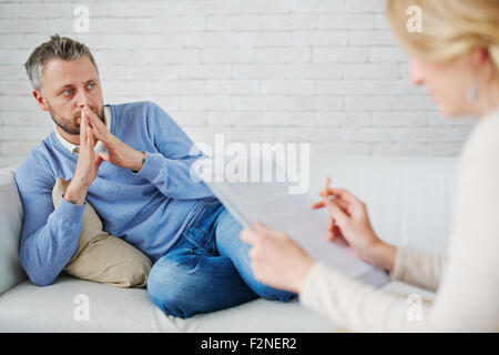Thoughtful man sitting on sofa in front of his psychologist Stock Photo