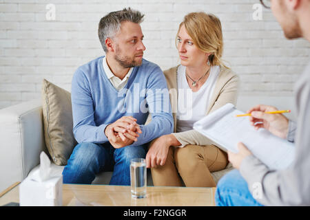 Sad couple sitting on sofa in front of psychologist Stock Photo