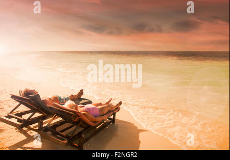 Older Caucasian couple relaxing on beach at sunset Stock Photo