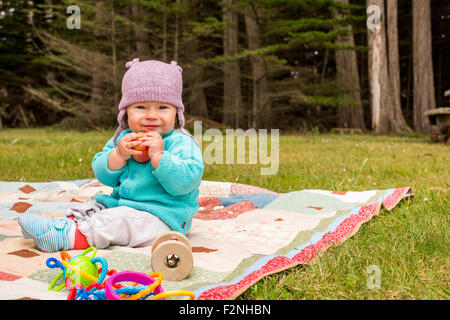 Caucasian baby girl sitting on blanket in grass Stock Photo