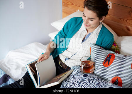 Woman drinking tea and reading in bed Stock Photo