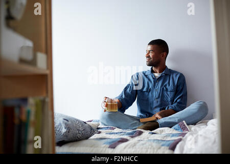 Black man drinking tea and reading on bed Stock Photo