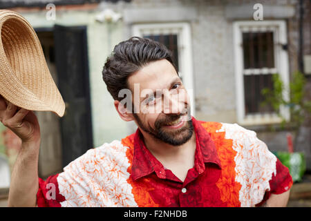 Caucasian man tipping straw hat in backyard Stock Photo