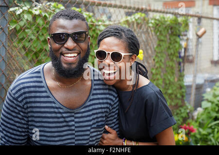 Smiling couple wearing sunglasses near fence Stock Photo