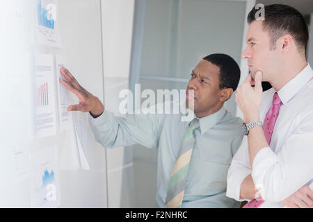 Businessmen examining charts on office wall Stock Photo
