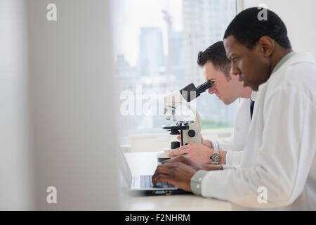 Scientists using laptop and microscope in lab Stock Photo