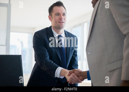 Businessmen shaking hands at desk in office Stock Photo