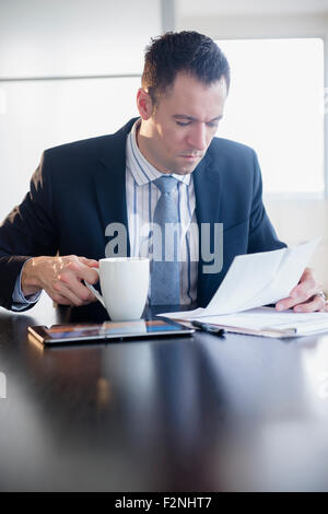 Businessman drinking coffee and reading paperwork Stock Photo
