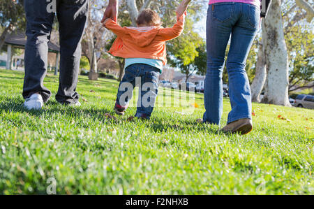Hispanic mother and father helping son walk in park Stock Photo