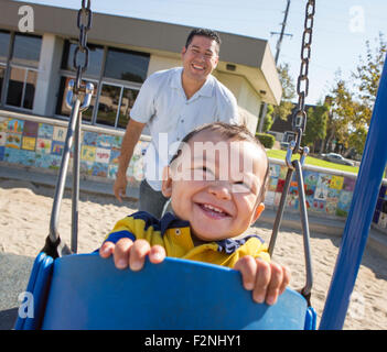 Hispanic father pushing son on playground swings