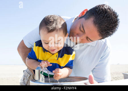 Hispanic father and son playing with water fountain Stock Photo