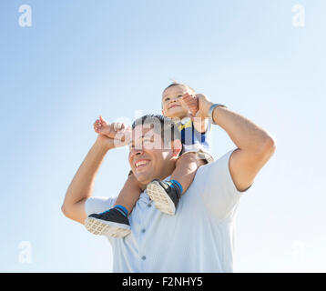 Low angle view of Hispanic father carrying son on shoulders Stock Photo