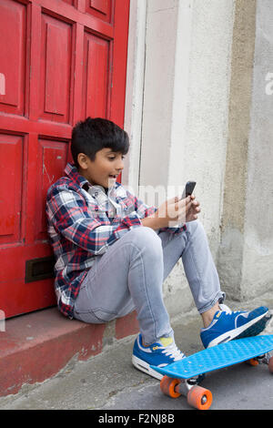 Asian boy with skateboard using cell phone Stock Photo