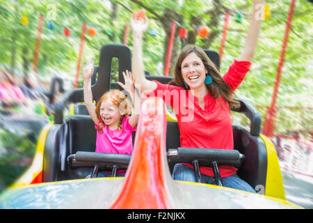 Mother and daughter riding roller coaster in amusement park Stock Photo