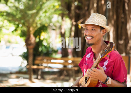 Hispanic musician playing ukulele in park Stock Photo