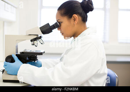 Mixed race scientist using microscope in laboratory Stock Photo