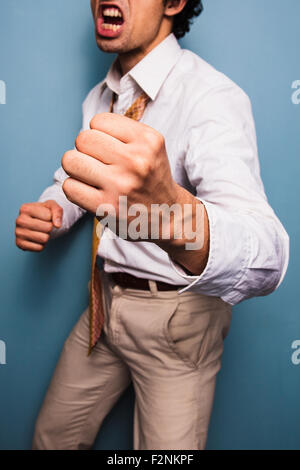 Young man standing by a blue wall is screaming and punching Stock Photo