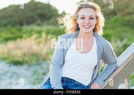 Smiling Caucasian woman sitting on banister over beach Stock Photo