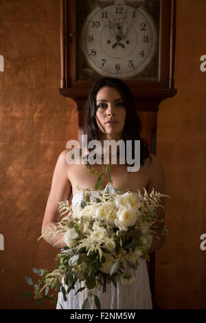 Bride holding bouquet of flowers under grandfather clock Stock Photo