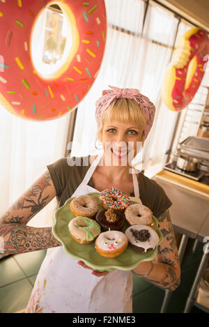 Asian baker holding plate of donuts in bakery Stock Photo