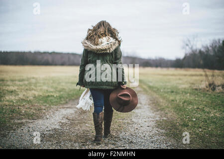 Caucasian woman walking on dirt path in rural field Stock Photo