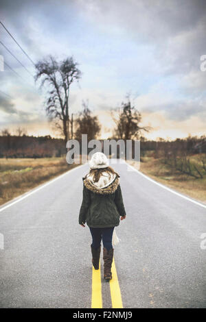 Caucasian woman walking on empty rural road Stock Photo