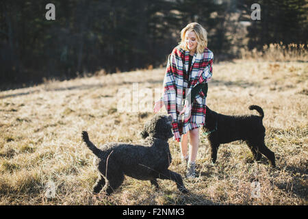 Caucasian woman playing with dogs in rural field Stock Photo