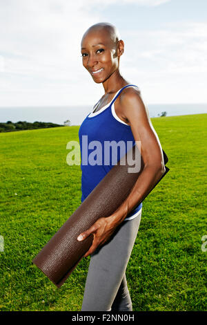 African American woman carrying yoga mat in park Stock Photo