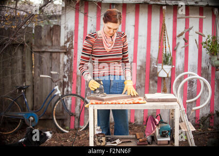 Woman sanding wood at table in backyard Stock Photo
