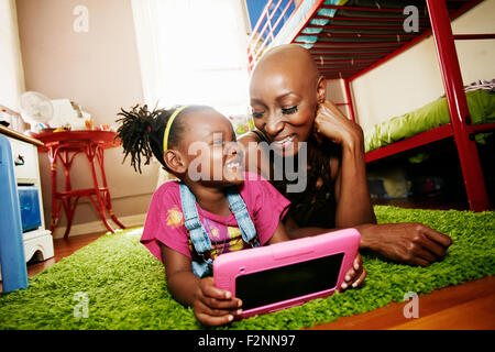 Black mother and daughter using digital tablet in bedroom Stock Photo