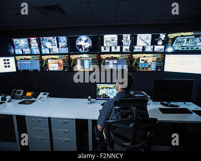 Hispanic security guard watching monitors in control room Stock Photo
