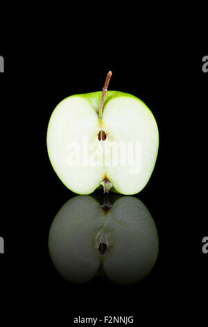 A cut green apple on a black reflective background. Stock Photo