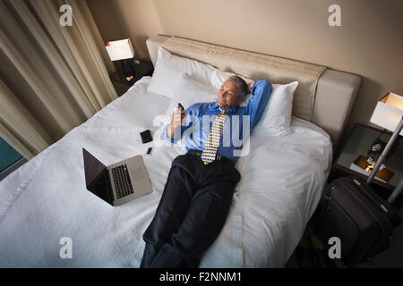 Caucasian businessman using cell phone on hotel bed Stock Photo