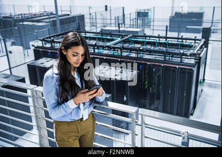 Mixed race businesswoman using cell phone on balcony over server room Stock Photo