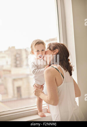 Caucasian mother kissing baby in window Stock Photo