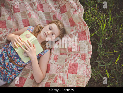Caucasian girl sleeping with book on blanket Stock Photo
