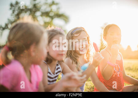 Girls eating flavored ice in sunny field Stock Photo