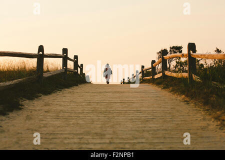 Silhouette of woman walking on wooden walkway Stock Photo