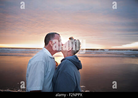 Caucasian couple kissing on beach at sunset Stock Photo