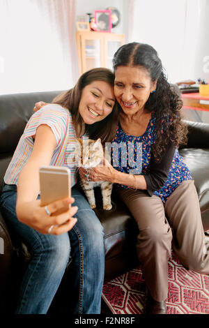 Grandmother and granddaughter taking selfie with cat on sofa Stock Photo